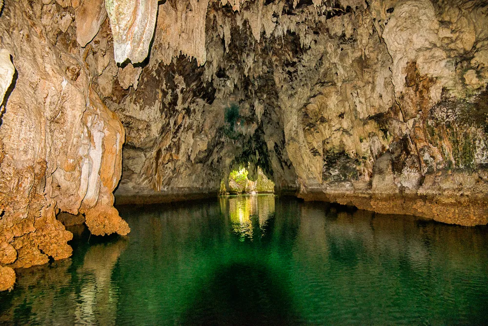 A limestone cave opening onto a green marine lake.
