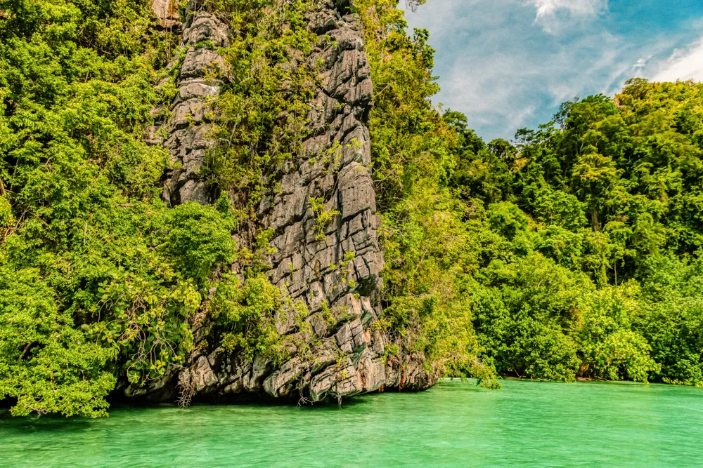 A karst tower covered in green above turquoise water.