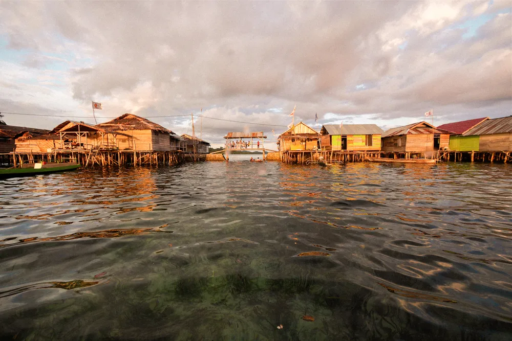 Stilt houses over shallow water at sunset.