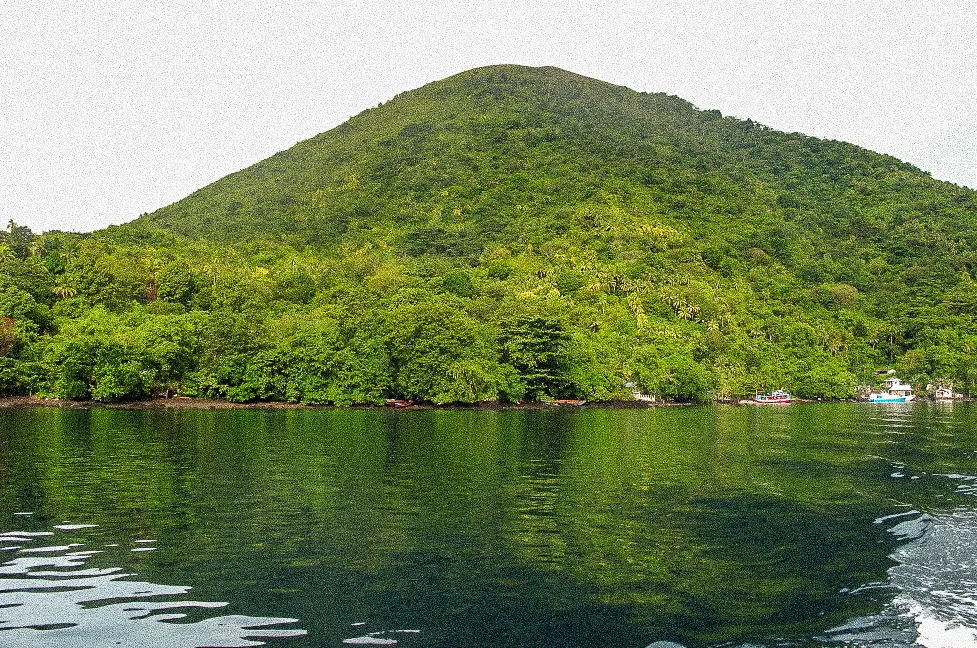 A green volcanic island rising from calm water.