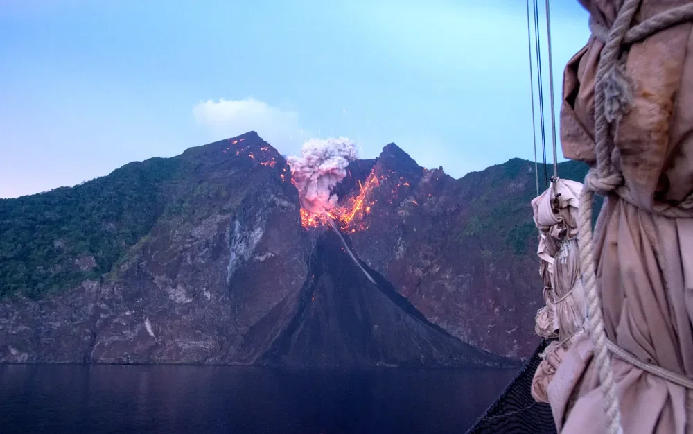 A volcano erupting above the water, seen from the boat.
