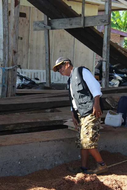 A man in a cap and vest walking past timber stacks at the shipyard