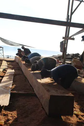 Workers kneeling on the long keel timber under the shipyard shelter