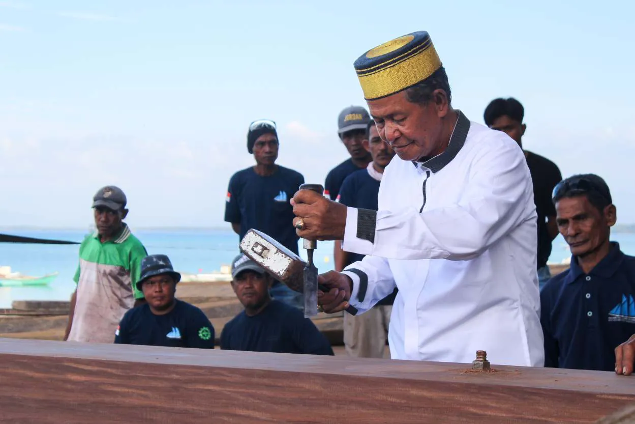 Pak Haji Wahab cutting a notch in the keel with mallet and chisel as workers look on