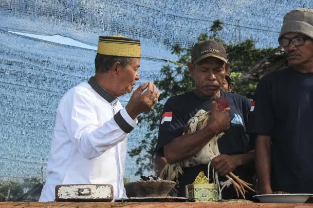 Pak Haji Wahab speaking beside a worker holding a rooster during the ritual