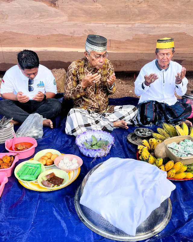 Pak Haji Wahab and two men seated in prayer around the offerings