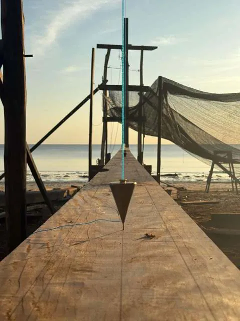 A plumb bob hanging over the ironwood keel at the shipyard, sea in the background