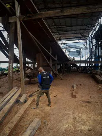 A shipwright walking under the hull frame in the building shed