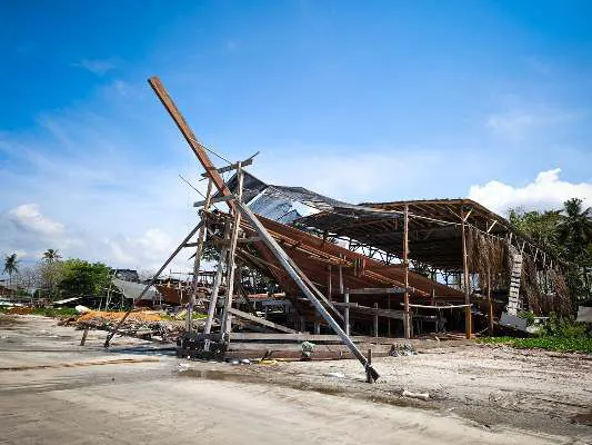 The WAOW 2 hull and its stem post in the shipyard shed under a blue sky