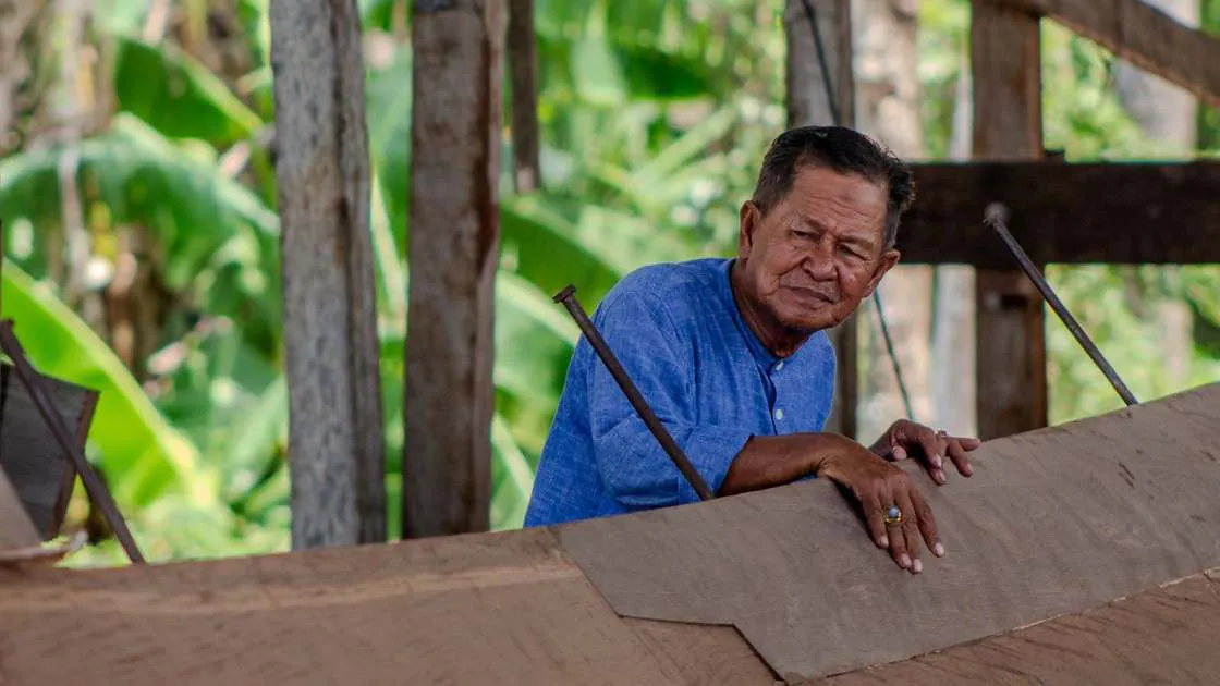An elderly master shipwright leaning on the hull planking