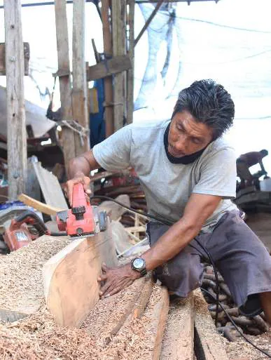 A carpenter planing a plank with an electric plane