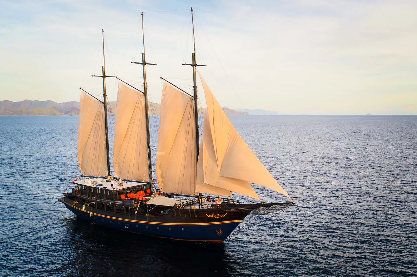 A three-masted phinisi anchored in a calm bay among forested limestone islands
