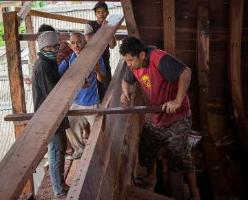 A group of shipbuilders fitting a plank inside the hull