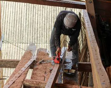 A shipbuilder cutting a plank with a power tool