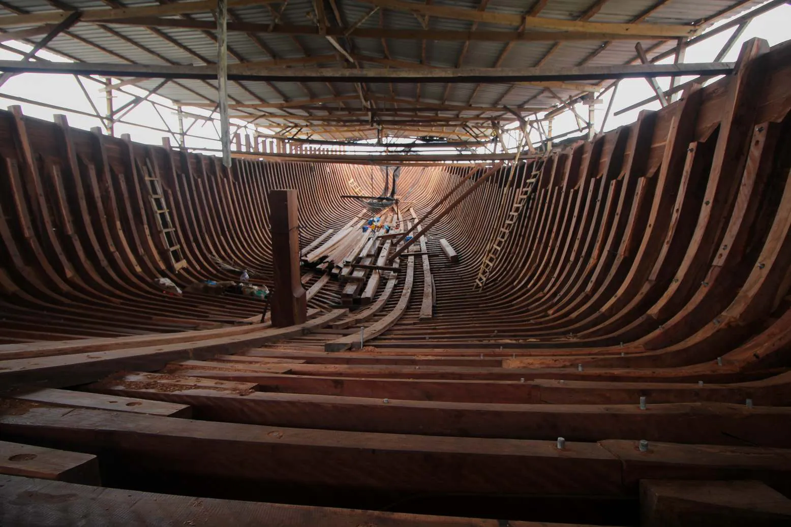 Wide view inside the hull of WAOW 2 toward the bow under the shipyard roof