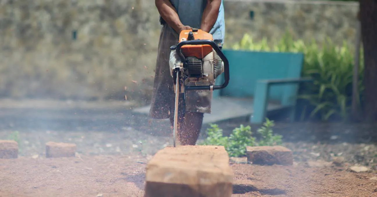 A shipbuilder cutting a timber block with a chainsaw