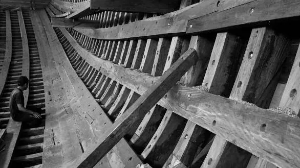 Black-and-white view of the hull's ribs with a worker sitting inside