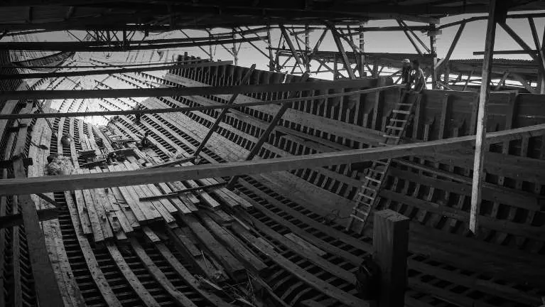 Black-and-white wide view inside the hull with timber stacked along the keel