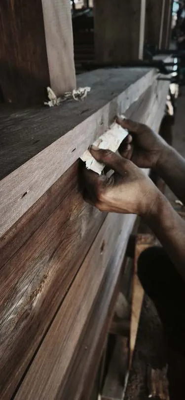 A hand placing caulking fibre along a plank seam