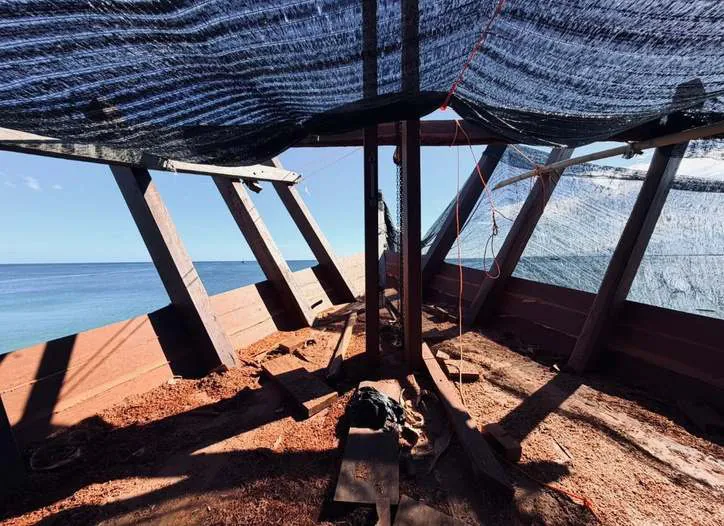 Inside the hull of WAOW 2 under shade netting, with a view of the sea