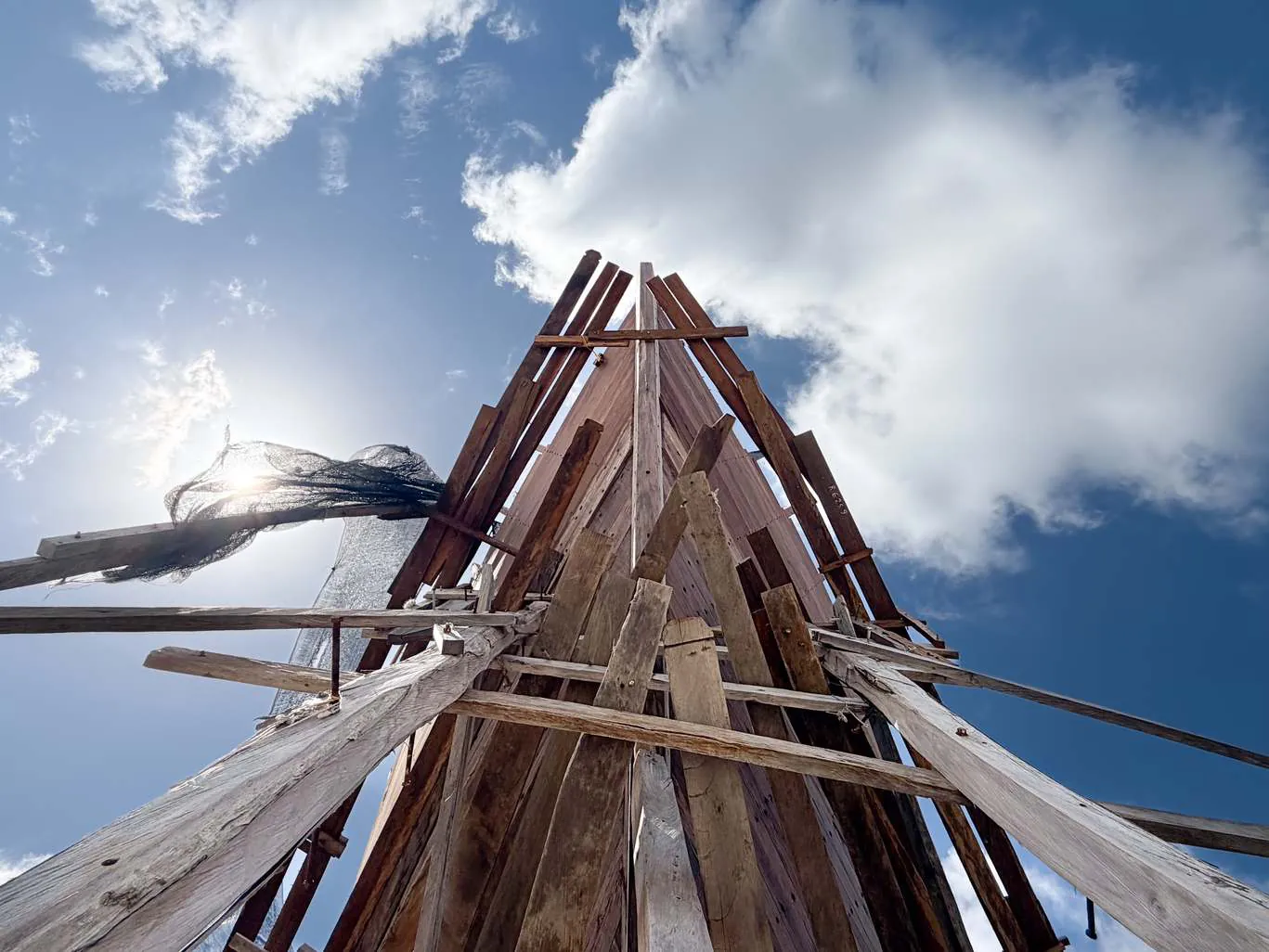 The wooden frames of WAOW 2 seen from below, rising against a blue sky with clouds