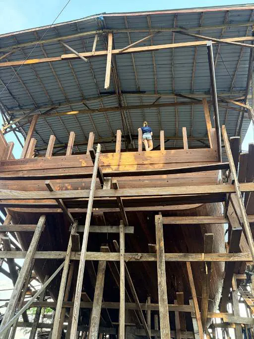 Camille standing high on the hull of WAOW 2 under the shipyard roof
