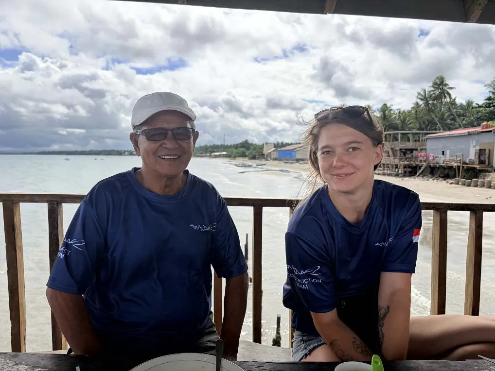 Camille and a shipyard craftsman in matching WAOW shirts on a terrace by the sea