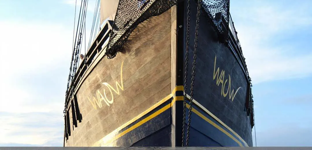 Bow of the WAOW with its name painted on the dark hull, seen from below against a blue sky