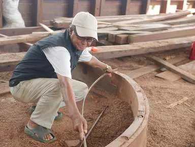 A man crouching to measure a curved wooden section