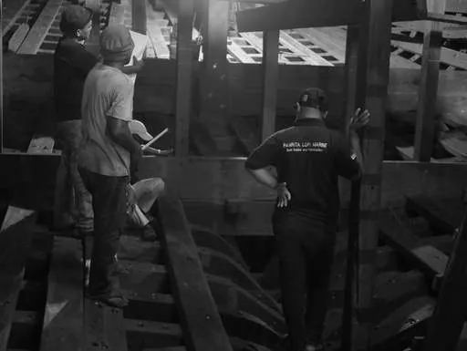Black-and-white photo of team members checking measurements inside the hull