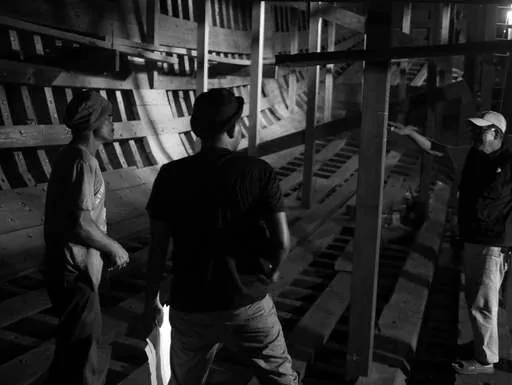 Black-and-white photo of three men discussing inside the hull