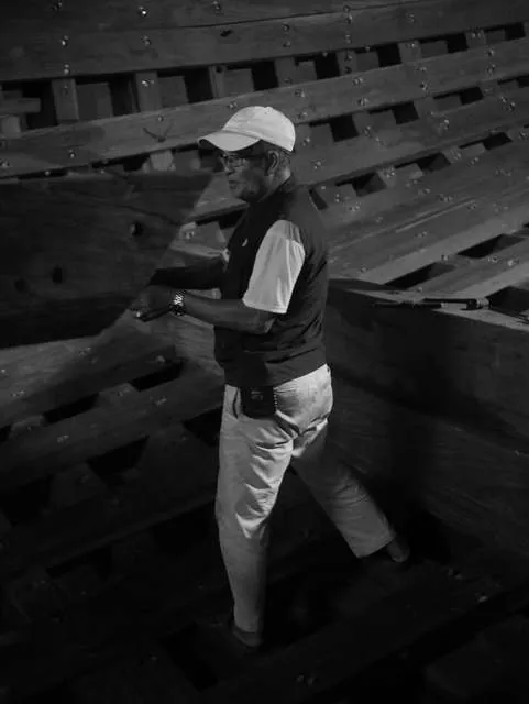 Black-and-white photo of a man in a cap measuring a frame inside the hull