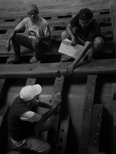 Black-and-white photo of three men reviewing plans in the hull