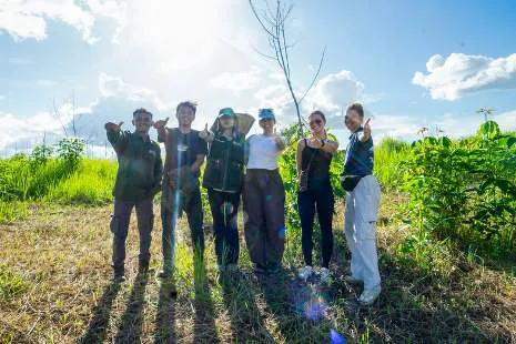 A group of people standing at a tree-planting site in a sunny field